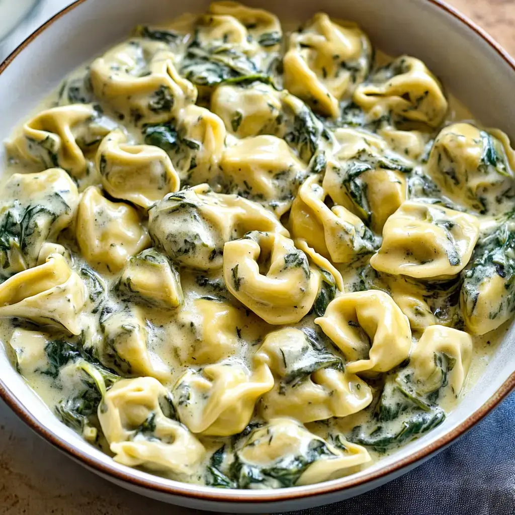 A bowl of tortellini pasta mixed with creamy sauce and spinach.