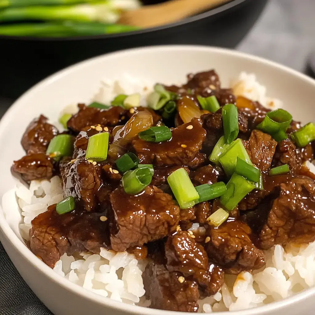 A bowl of white rice topped with tender pieces of beef in brown sauce and garnished with green onions.