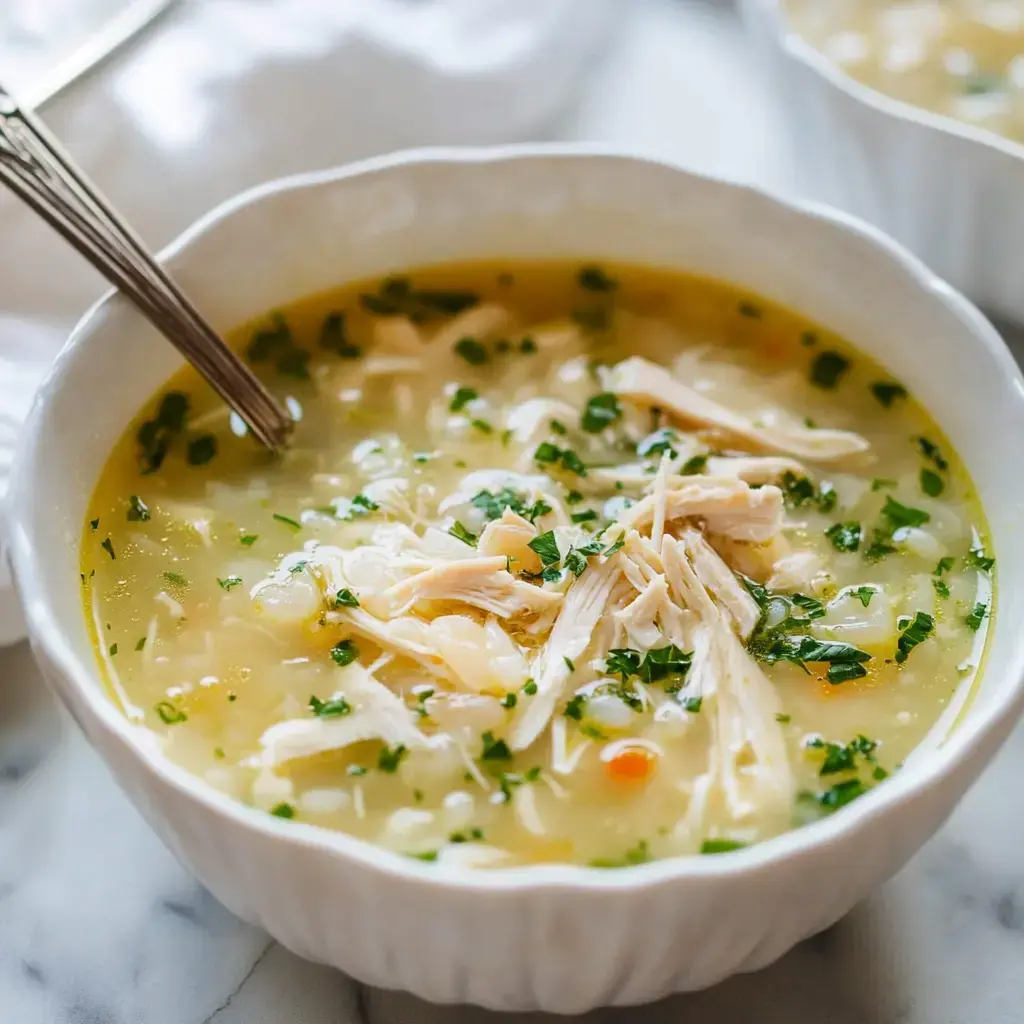 A bowl of chicken soup with shredded chicken and chopped parsley on top.