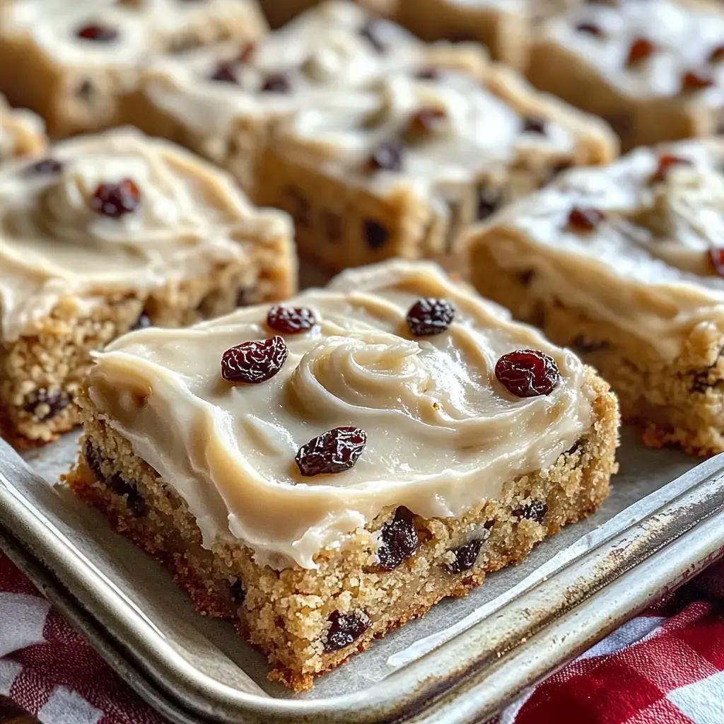 A close-up of dessert squares topped with creamy frosting and garnished with raisins.