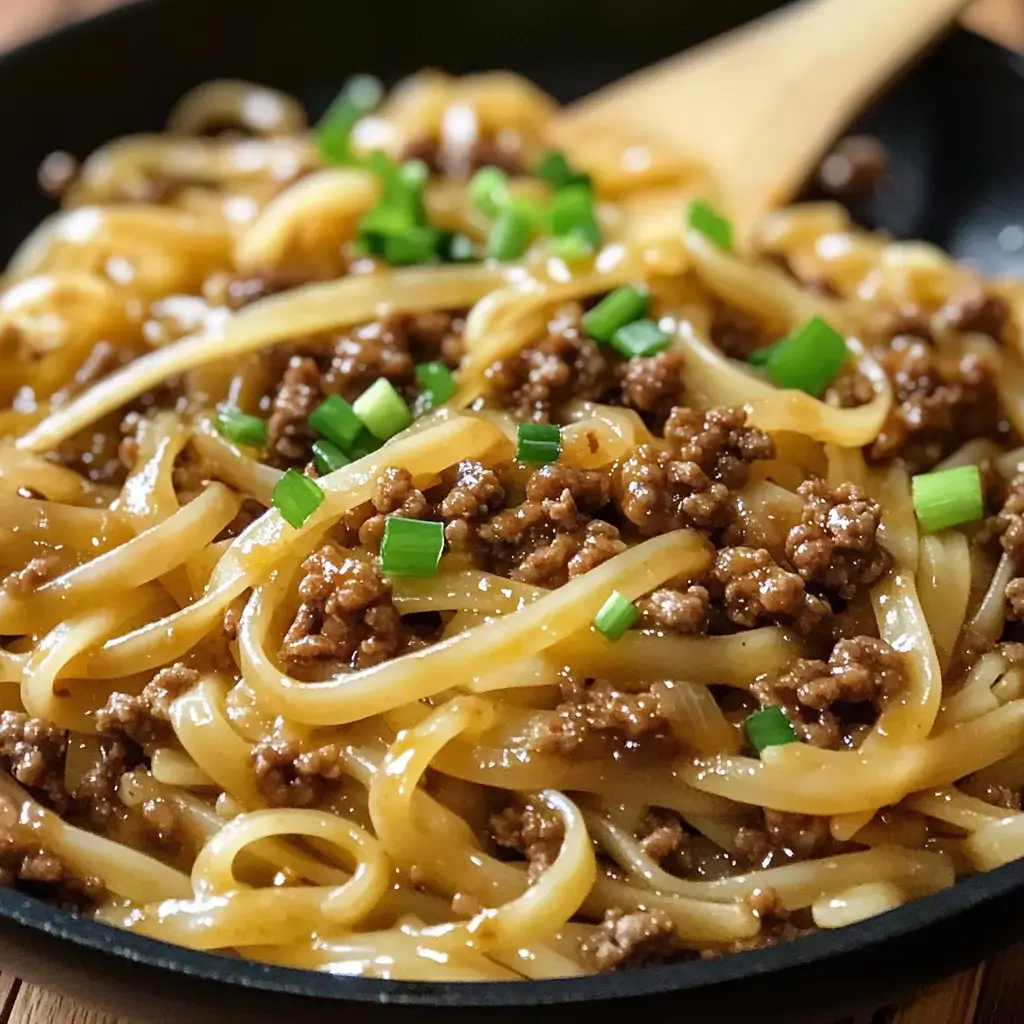 A close-up of a dish featuring cooked noodles topped with ground meat and garnished with green onions.