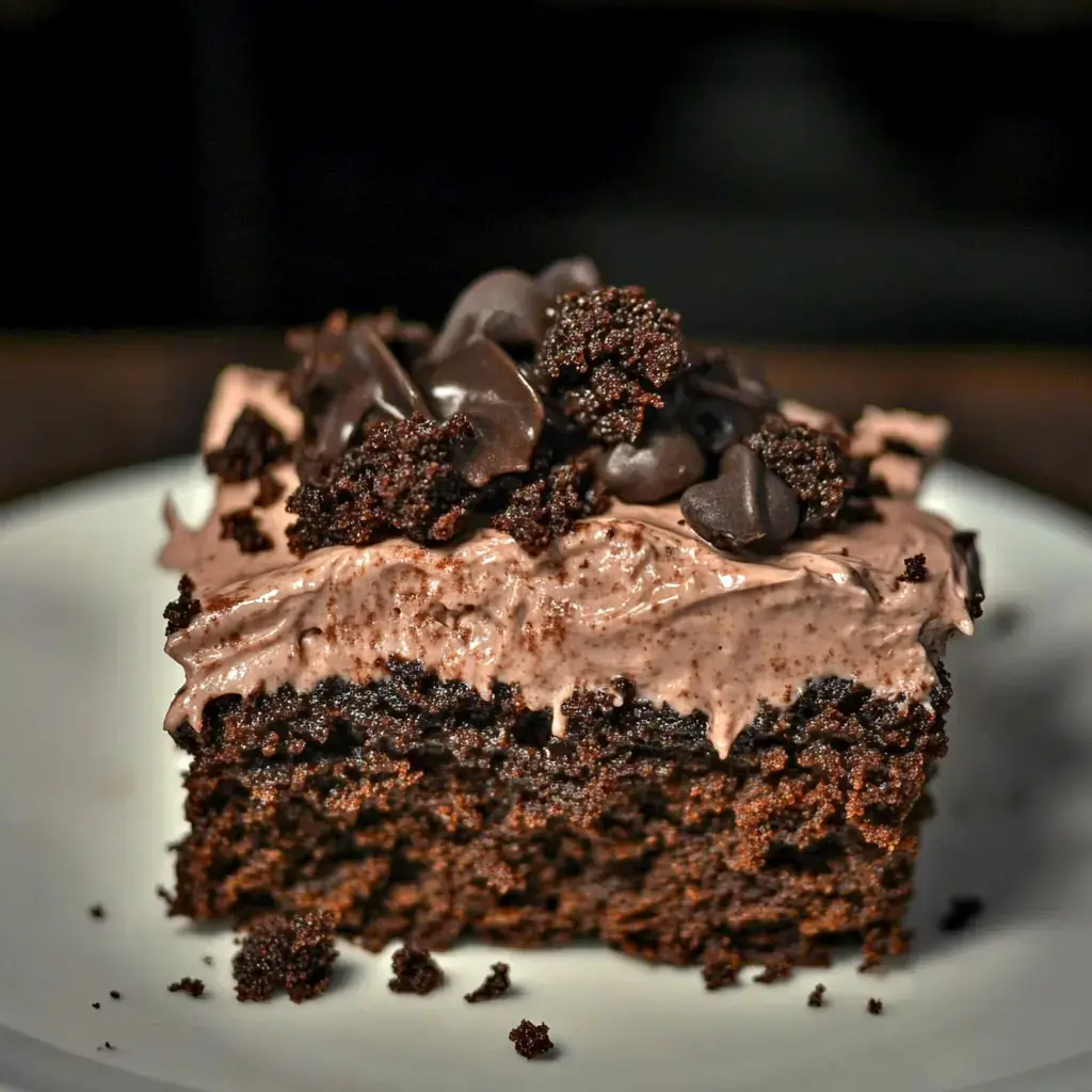 A slice of chocolate cake topped with chocolate frosting and chocolate crumbles is displayed on a white plate.