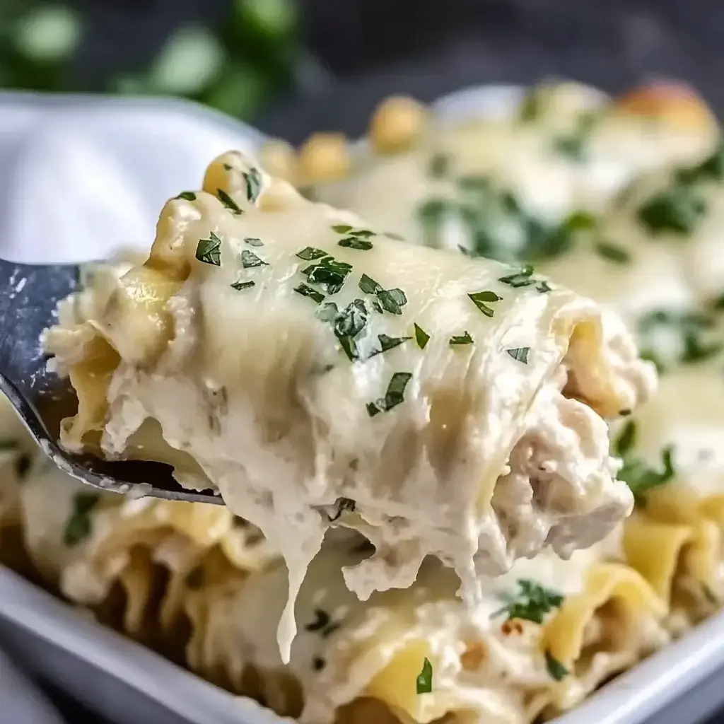 A fork holds a creamy chicken pasta dish topped with parsley, with more servings visible in the background.