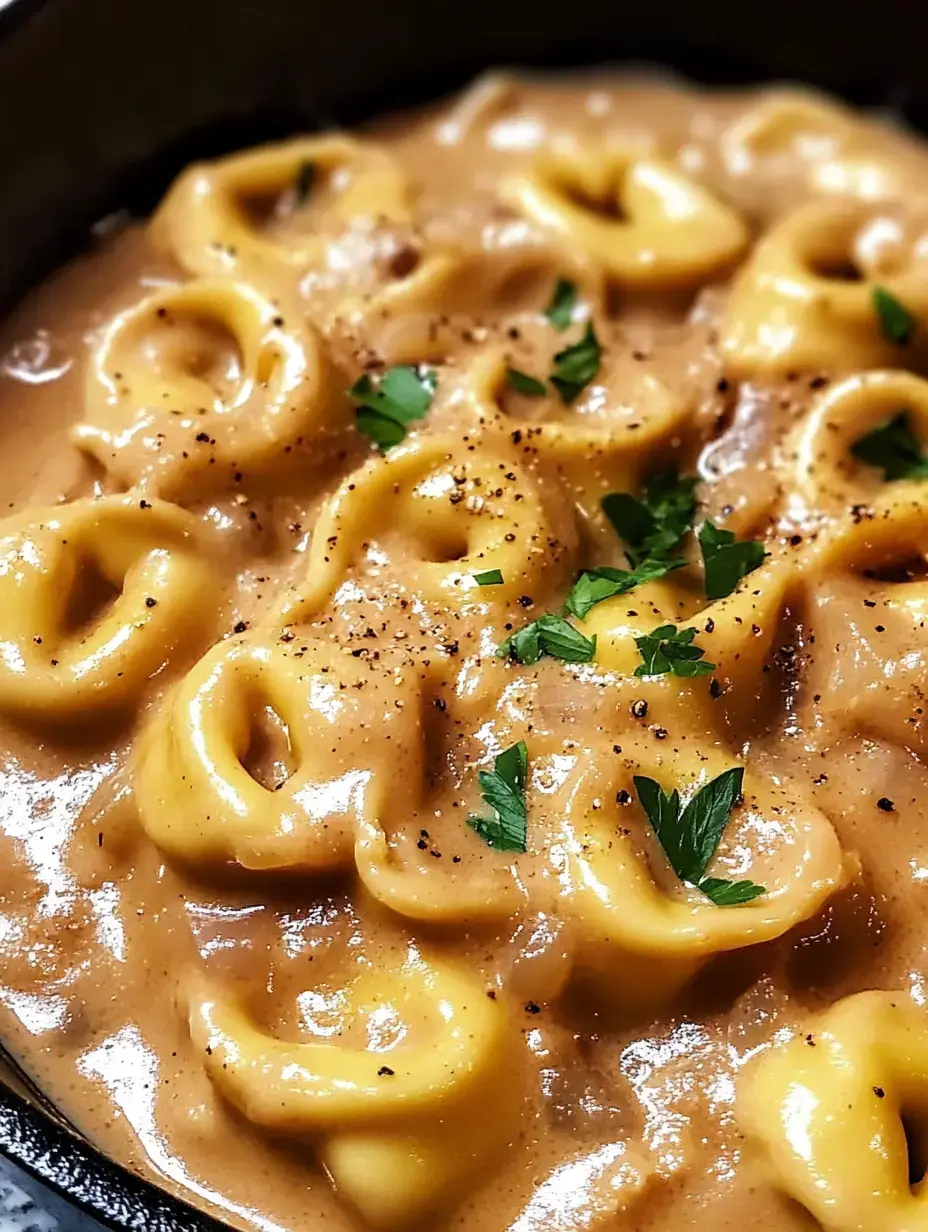 A close-up view of pasta in a creamy sauce, garnished with parsley and black pepper.