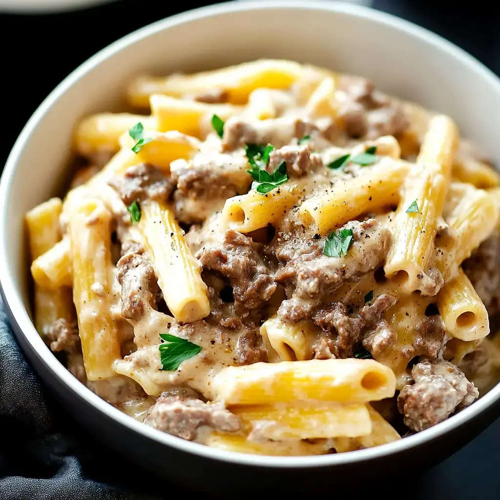 A bowl of creamy pasta, featuring rigatoni mixed with ground beef and garnished with parsley.