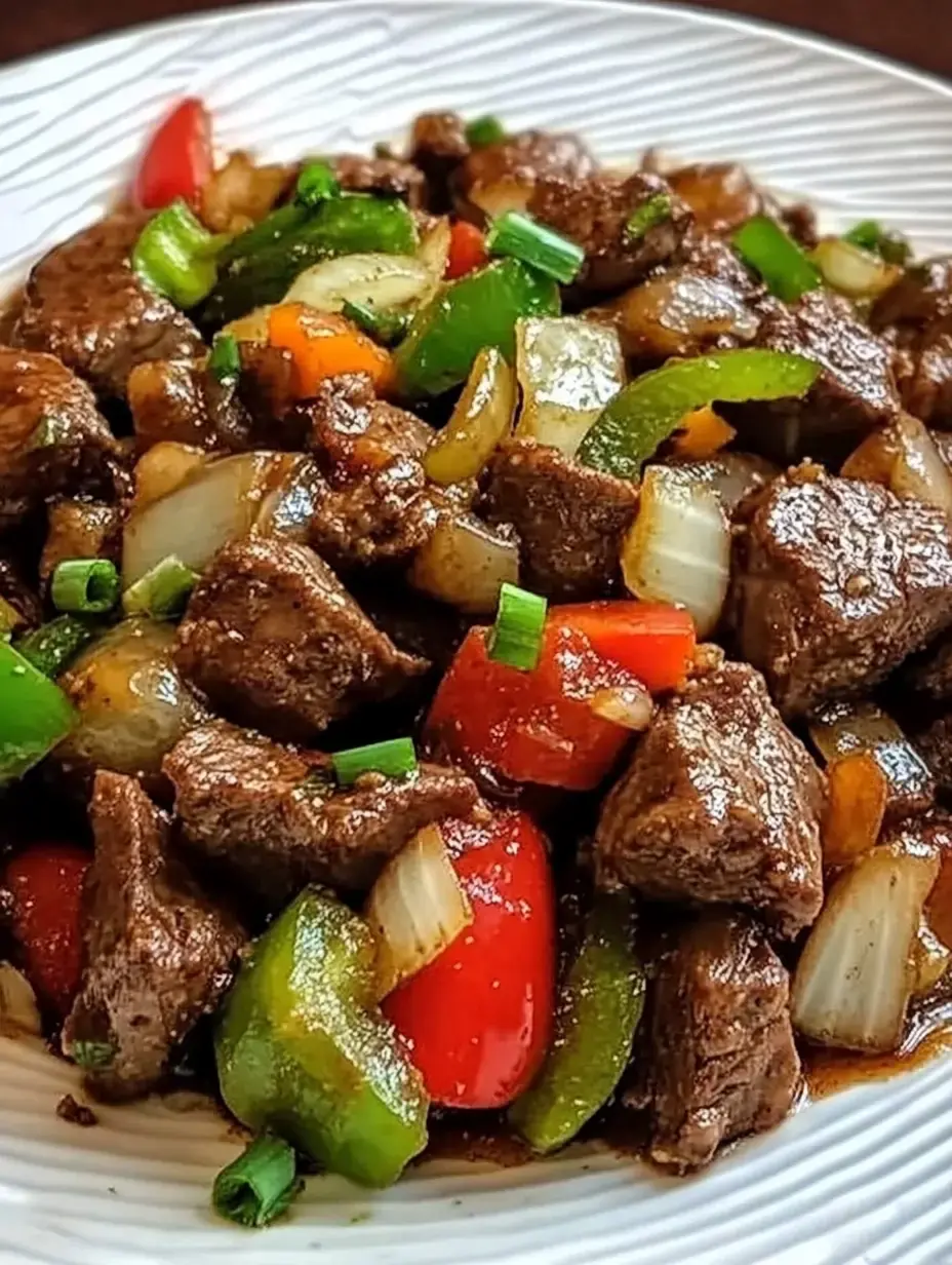 A close-up of a plate featuring chunks of beef sautéed with colorful bell peppers, onions, and green onions in a savory sauce.