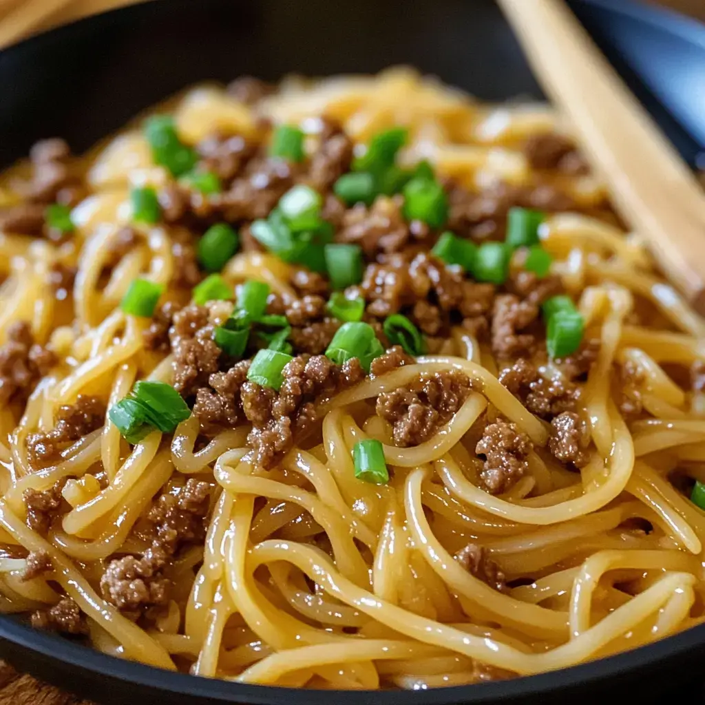 A close-up view of a bowl of noodles topped with ground meat and green onions.