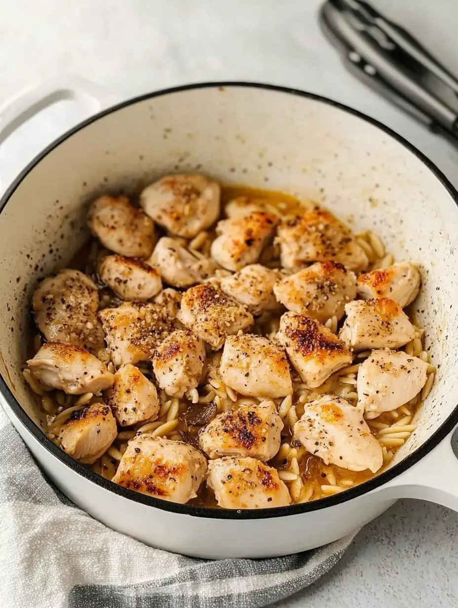 A pot filled with cooked chicken pieces and orzo pasta, seasoned with spices and garnished, sitting on a checked kitchen towel.