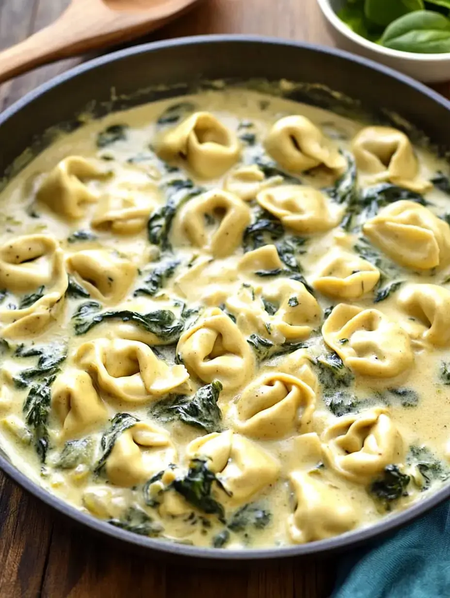 A skillet filled with creamy tortellini pasta mixed with fresh spinach in a rich sauce.