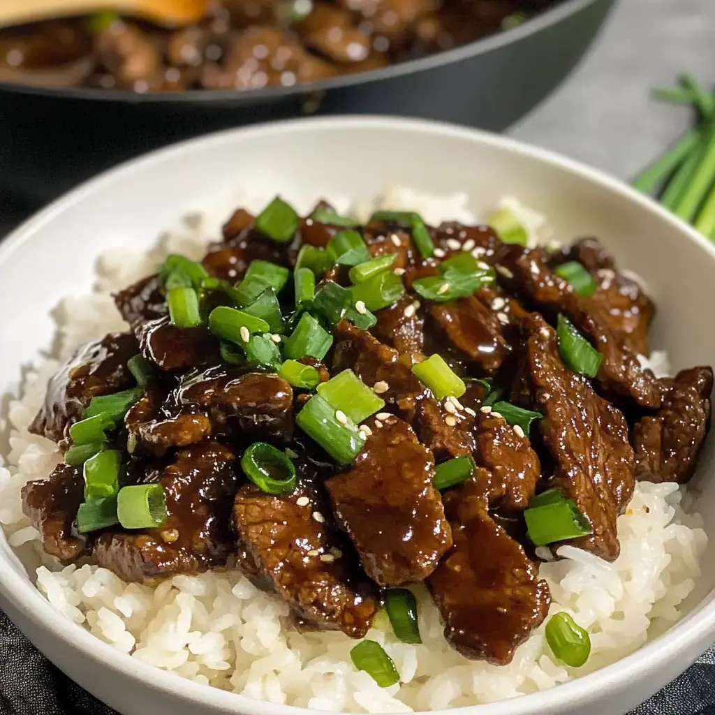 A bowl of white rice topped with sautéed beef and garnished with chopped green onions and sesame seeds.