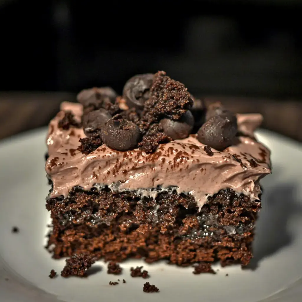 A slice of chocolate cake topped with creamy frosting and dark chocolate crumbs.