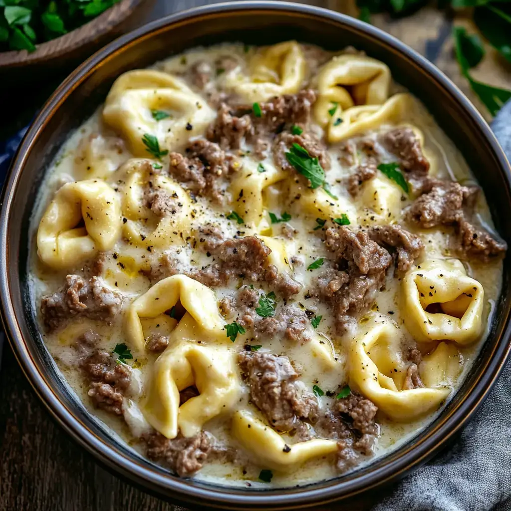 A bowl of creamy tortellini soup with ground beef and garnished with fresh parsley.
