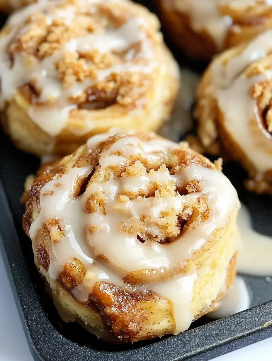 A close-up image of freshly baked cinnamon rolls drizzled with icing and topped with crumbs in a baking tray.