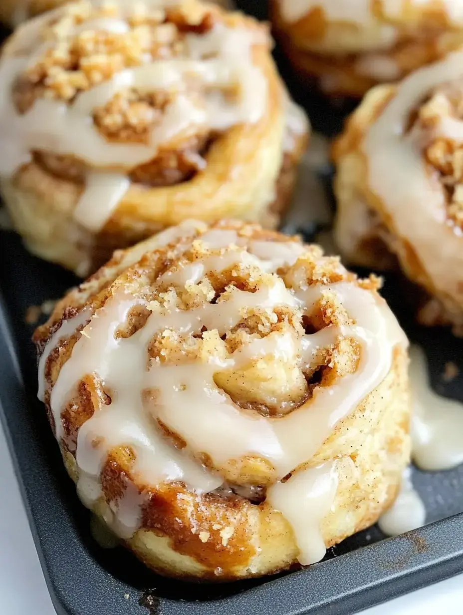 A close-up image of freshly baked cinnamon rolls topped with a creamy glaze and sprinkled with crumbs, arranged in a baking tray.