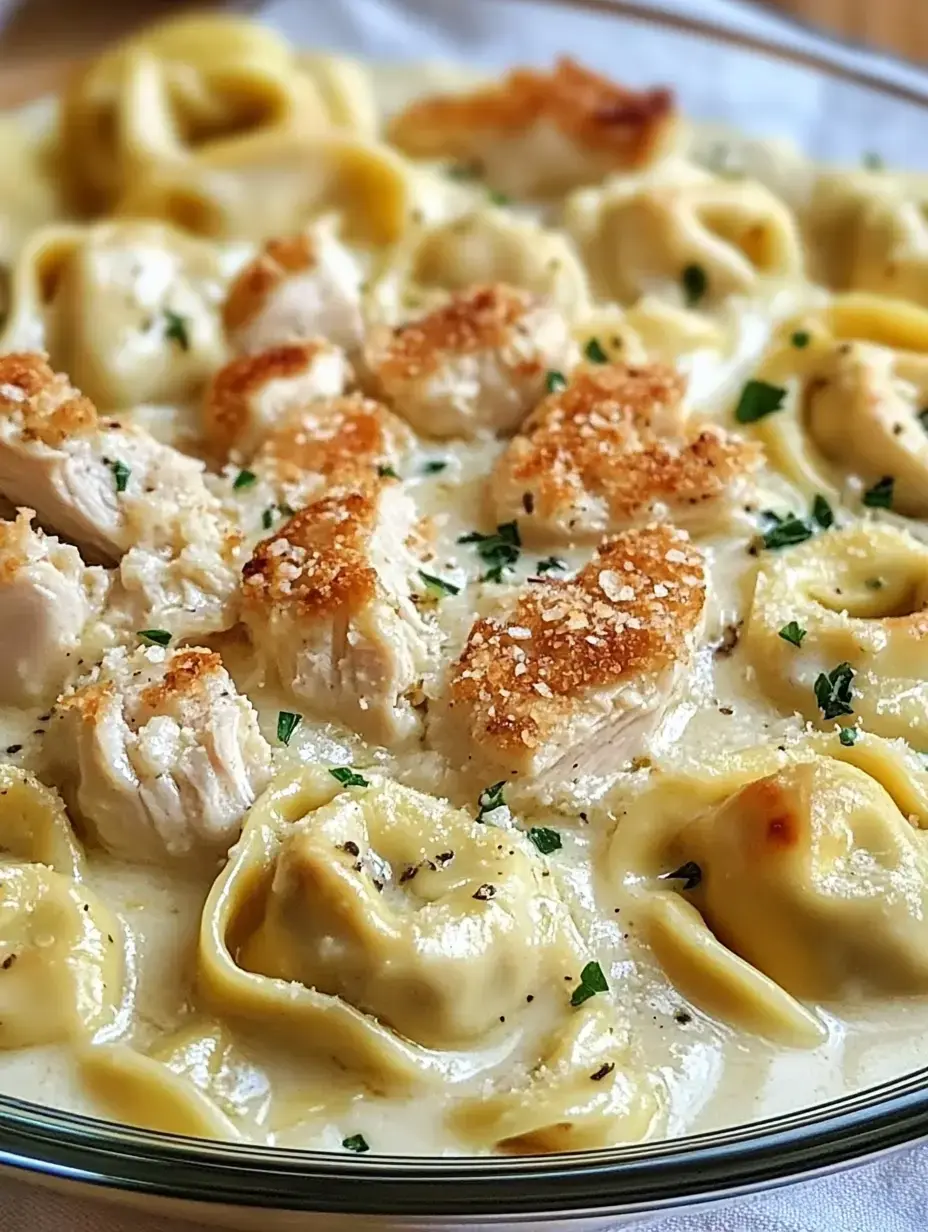 A creamy pasta dish featuring golden-brown chicken pieces and cheese-filled tortellini garnished with parsley.