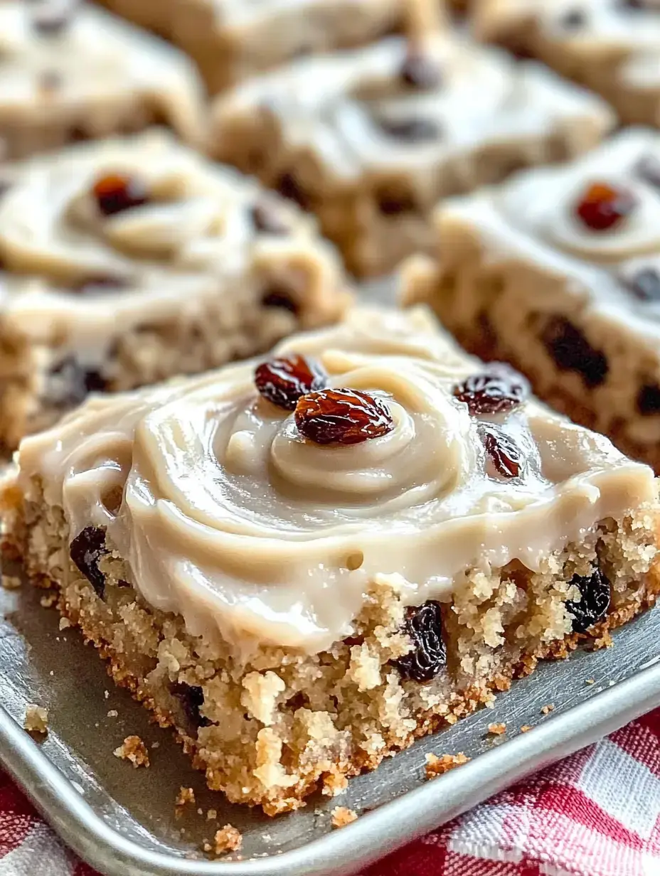 A piece of moist cake topped with swirled frosting and decorated with raisins, sitting on a silver tray.