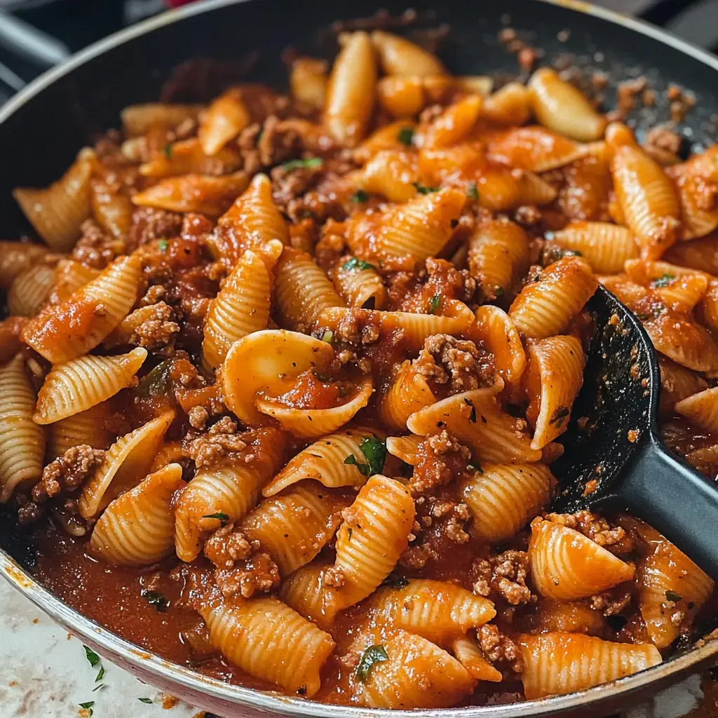 A close-up view of a skillet filled with pasta shells mixed with ground meat in a tomato sauce.