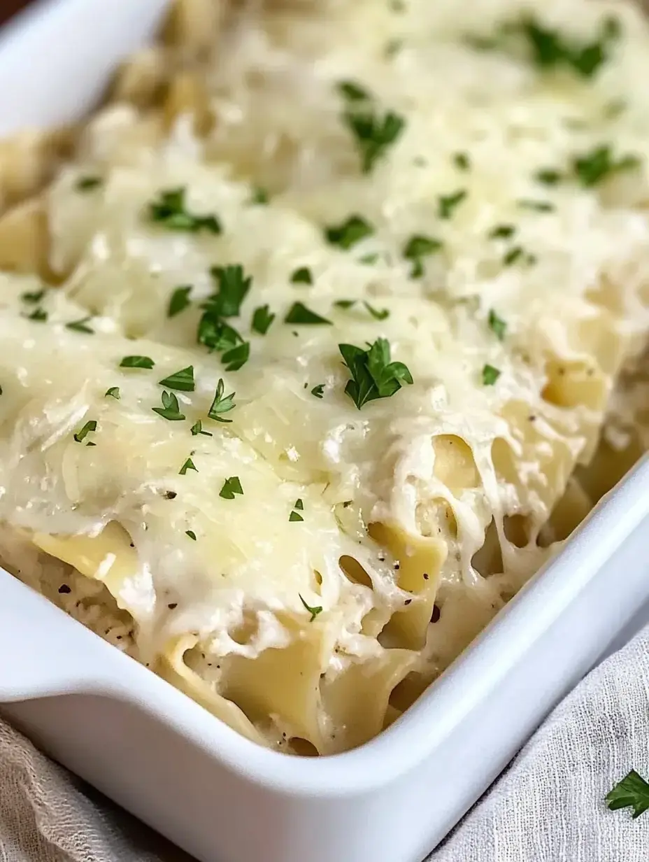 A close-up view of a creamy pasta dish topped with melted cheese and garnished with chopped parsley, served in a white baking dish.