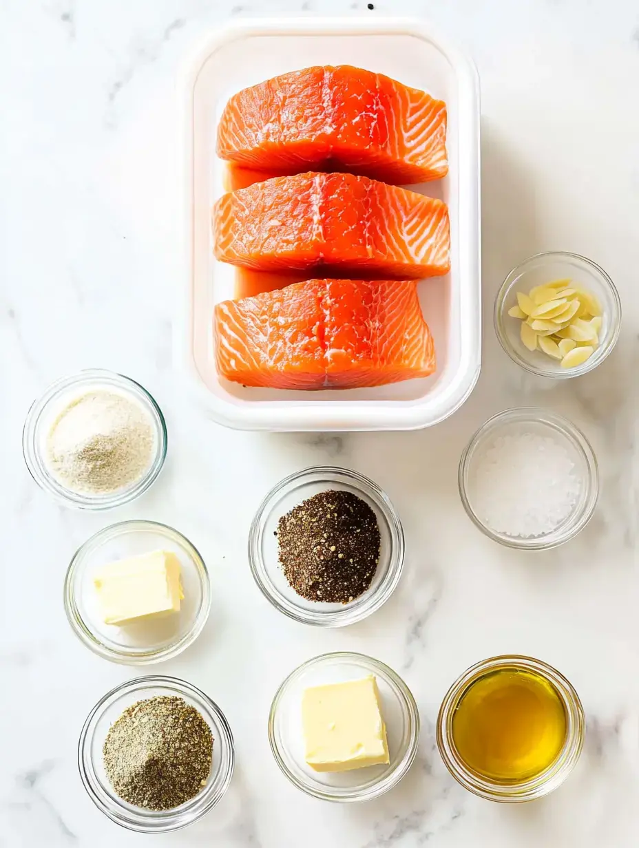 Three pieces of fresh salmon fillet are arranged in a container, surrounded by small bowls of various seasonings and ingredients, including butter, olive oil, salt, pepper, and almonds.