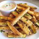 A plate of fried zucchini with a bowl of dipping sauce.
